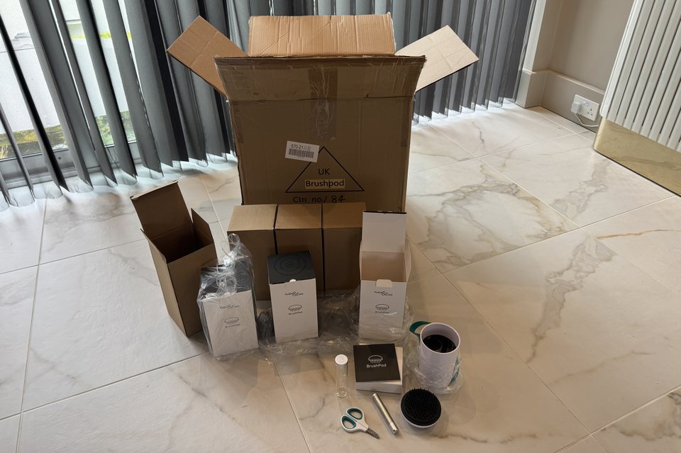 An opened BrushPod outer trade case with inner cartons stacked in front of it and a single unit unpacked to one side